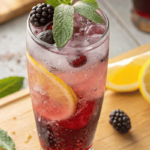 Homemade blackberry sage lemonade refresher in tall iced glass with lemon and sage
