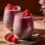Two glasses of raspberry chia seed smoothie layered with chia pudding and topped with fresh raspberries.